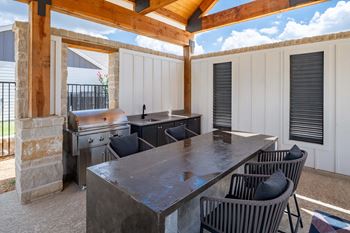 an outdoor kitchen with a table and chairs and a grill